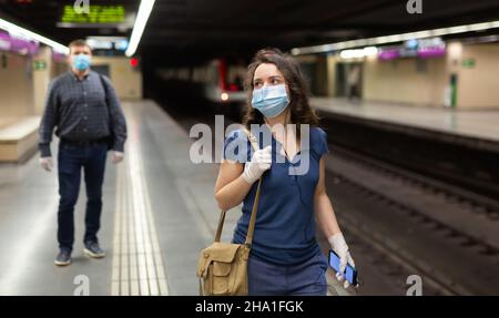 Frau in Gesichtsmaske und Ohrhörer auf U-Bahn-Plattform Stockfoto