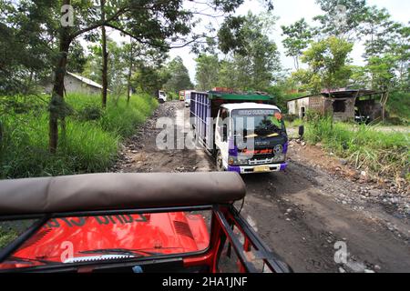 Auf einer Jeep-Tour durch den Berg Merapi in der Nähe von Yogyakarta in Zentral-Java, Indonesien, passieren schwere Lastwagen mit vulkanischem Gestein. Stockfoto