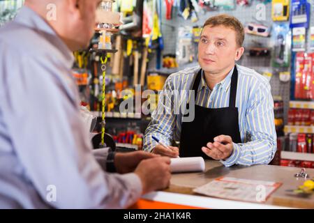 Verkäufer, der dem Mann im Geschäft Werkzeuge anbietet Stockfoto