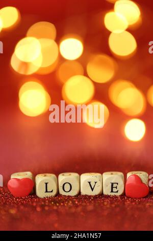 Liebe und Beziehung.Valentinstag.schöne festliche leuchtenden Hintergrund. Inschrift Liebe aus Holzbuchstaben auf rotem Glitzer-Hintergrund mit Stockfoto
