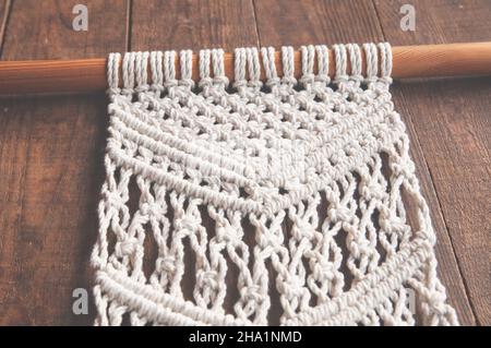 Weberei aus Baumwollfäden Dekorationsarbeit aus 100% Baumwolle im Stil von Macrame handgefertigt auf einem Holzhintergrund. Frauenhobby. Stockfoto
