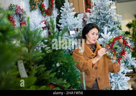 Selbstbewusste asiatische Frau wählt einen Weihnachtskranz Stockfoto