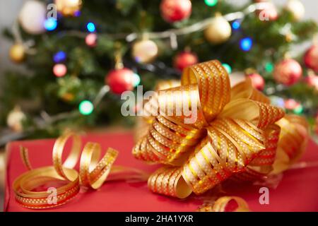 Nahaufnahme einer Geschenkbox, die an Weihnachten oder Neujahr mit einer goldenen Schleife unter einem Weihnachtsbaum verziert ist. Stockfoto