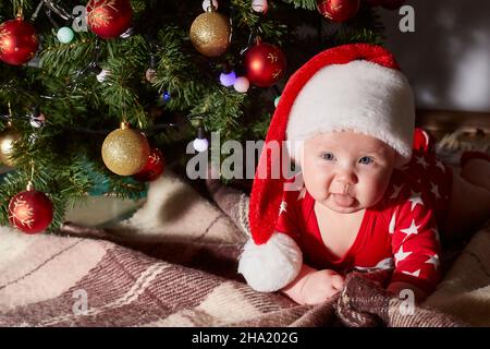 Kaukasisches Baby zeigt seine Zunge und kriecht zu Hause unter dem Weihnachtsbaum. Lifestyle. Copy space. Stockfoto