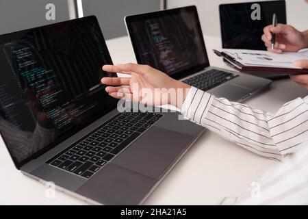 Co-Working-Konzept die Frau trägt eine weiße, vertikal gestreifte Bluse, die das Thema auf ihrem Computer berichtet, während ihr Partner es auf den Pap schreibt Stockfoto