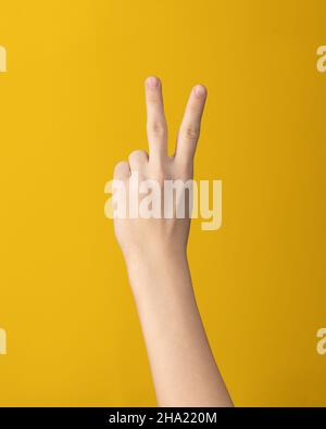Weibliche Handbewegung zeigt zwei Finger Index und Mitte auf gelbem Hintergrund isoliert Stockfoto