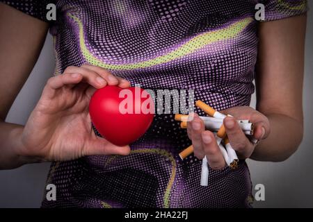 Rauchen aufhören und Herzgesundheit Konzept. Frau mit einem Gummiherz und einem Haufen zerrissener Zigaretten. Stockfoto