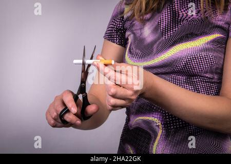 Frau schneidet eine Zigarette mit einer Schere. Rauchen aufhören und Gesundheitskonzept. Stockfoto