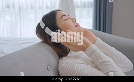 Frau trägt kabellose Kopfhörer Genießen Sie gute meditative Musik. Gelassene junge Frau im Headset Entspannen Sie sich beim Hören eines Hörbuchs mit geschlossenen Augen. Stockfoto