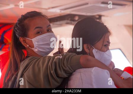 2 Frauen, inländische Touristen, (1 Kambodschaner, links, 1 gemischte Rassen, Rechts, 1/4 Vietnamesen, 1/4 Cham, 1/4 Chinesen und 1/4 Kambodschaner), mit schützenden Gesichtsmasken, fahren Sie mit der Fähre nach Saracen Bay, Koh Rong Samloem während der COVID - Pandemie 19. Provinz Sihanoukville, Kambodscha. 6th. Dezember 2021. © Kraig Lieb Stockfoto