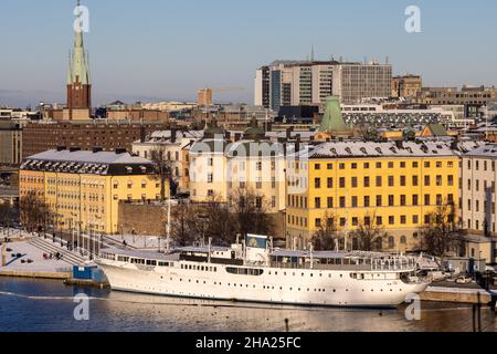 Panorama der Stadt Stockholm an einem sonnigen Wintertag vom Hügel aus fotografiert. St. Clare's Church, bunte Häuser in der Nähe und ein Boot vor dem Hotel. Stockfoto