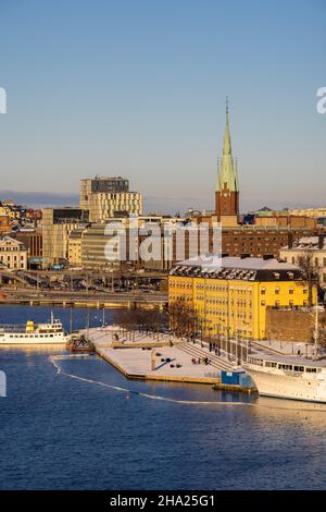 Panorama der Stadt Stockholm an einem sonnigen Wintertag vom Hügel aus fotografiert. St. Clare's Church, bunte Häuser in der Nähe und ein Boot vor dem Hotel. Stockfoto