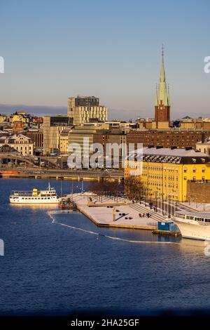 Panorama der Stadt Stockholm an einem sonnigen Wintertag vom Hügel aus fotografiert. St. Clare's Church, bunte Häuser in der Nähe und ein Boot vor dem Hotel. Stockfoto