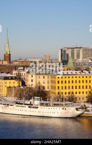 Panorama der Stadt Stockholm an einem sonnigen Wintertag vom Hügel aus fotografiert. St. Clare's Church, bunte Häuser in der Nähe und ein Boot vor dem Hotel. Stockfoto