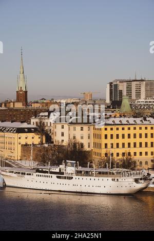 Panorama der Stadt Stockholm an einem sonnigen Wintertag vom Hügel aus fotografiert. St. Clare's Church, bunte Häuser in der Nähe und ein Boot vor dem Hotel. Stockfoto