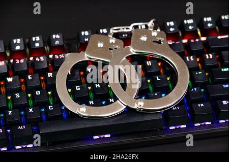 Tastatur und Handschellen mit LED-Leuchten an. Konzept der Cyberkriminalität Stockfoto