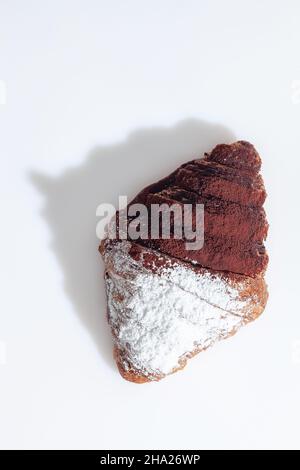 Schokoladencroissant, bestreut mit Puderzucker und Kakao auf weißer Oberfläche Stockfoto