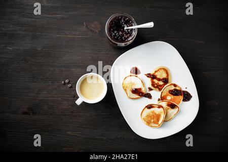 Pfannkuchen mit Marmelade und Kaffeetasse auf Holztisch Hintergrund. Flach liegend. Stockfoto