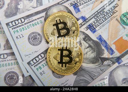 Draufsicht auf zwei Bitcoin-Goldmünzen, die auf frischen 100-Dollar-US-Scheinen liegen Stockfoto