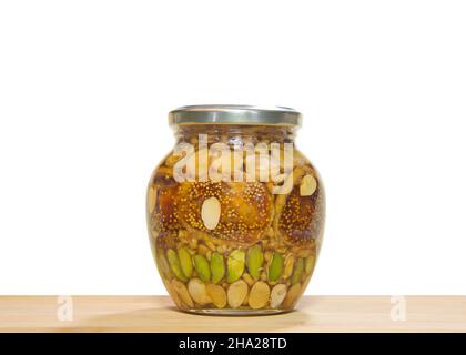 Glas mit Nüssen und Früchten in einem Glas Honig konserviert. Pistazien, Walnüsse, Erdnüsse, Mandeln und Feigen. Glas auf einem hellen Holztisch isoliert auf weiß. Stockfoto