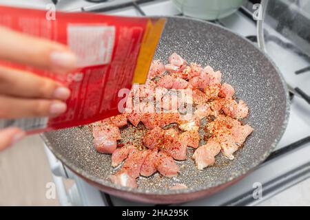 Hausfrau gießen Würze in Fisch oder Geflügelfleisch in einer Pfanne gebraten. Paprika und roter Pfeffer als Aromazutat Stockfoto