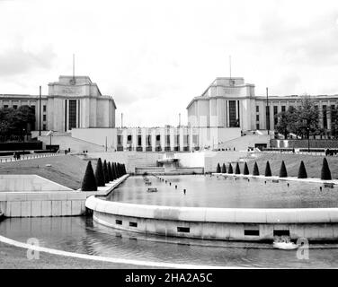 Blick auf den Modernen Palais de Chaillot im Hintergrund mit dem Brunnen der Gärten des Trocadero im Vordergrund. Das Foto wurde um den 1. März 1945 gemacht. Die Kameraposition befindet sich links von der Mitte am Fuß des Pools und der Blick ist nach Nordwesten. Der Brunnen sprüht nicht und es gibt kleine Gruppen von Menschen, die den Brunnenbereich besuchen. Nur das Zentrum des viel breiteren Palais ist auf dem Foto zu sehen, und viele weitere Besucher schauen offensichtlich auf die Ebene des Palais. Die Fotografin Clarence Inman war von Ende November 1944 bis Ende Mai 1945 in Paris stationiert. Stockfoto