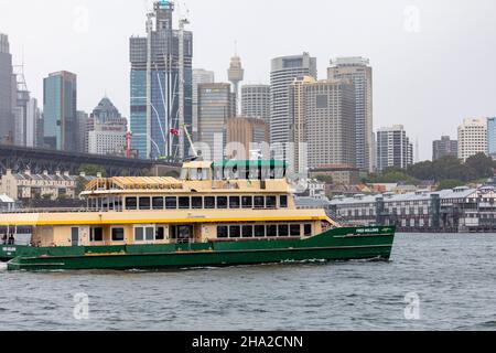 Sydney Ferry MV Fred hohlt an einem düsteren und nassen Sommertag in Sydney, NSW, Australien durch hohe Gebäude im Stadtzentrum von Sydney Stockfoto
