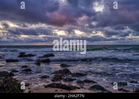 Landschaft, Meeresuntergang an der Küste von Huisduinen, Niederlande. Lange Darstellung der Wellen, dramatischer Himmel, detailliert, Algen, Felsen. Stockfoto