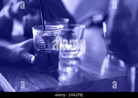 Nicht erkennbare Person, die am Tisch sitzt und am Sommertag einen kühlen Fruchtcocktail in der Cafeteria genießt, Farbe 2022 Jahre, sehr peri, getönt Stockfoto