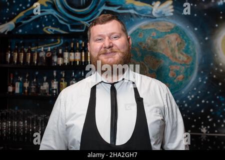 Bärtiger Erwachsener lustig positiv lächelnd kaukasisch aussehend professioneller Barkeeper Portrait im Nachtclub. Stockfoto