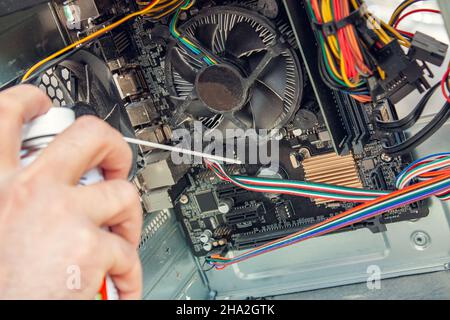 Wartung und Reinigung der Innenseiten des Computers. Die Hand des Mannes hält einen Zylinder mit Druckluft und reinigt die Innenseiten des Computers. Stockfoto