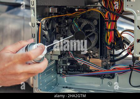 Wartung und Reinigung der Innenseiten des Computers. Die Hand des Mannes hält einen Zylinder mit Druckluft und reinigt die Innenseiten des Computers. Stockfoto