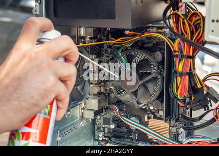 Wartung und Reinigung der Innenseiten des Computers. Die Hand des Mannes hält einen Zylinder mit Druckluft und reinigt die Innenseiten des Computers. Stockfoto