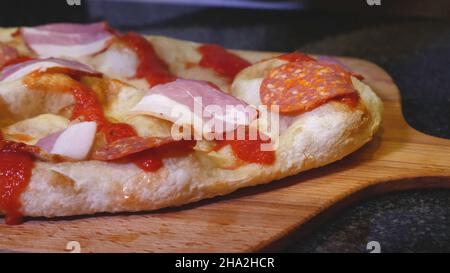 Der Küchenchef legt Schinkenscheiben auf die Pizza. Rahmen. Nahaufnahme Kochen saftige leckere italienische Pizza mit Schinken und Salami. Der Koch trägt Handschuhe und legt Mea-Scheiben Stockfoto