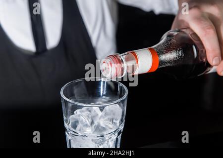 Die Hand eines professionellen Barkeeps gießt roten Sirup in ein Glas Eiswürfel. Der Prozess der Zubereitung eines alkoholischen Cocktails. Stockfoto