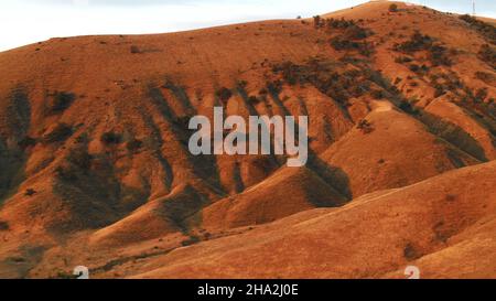 Schöne Aussicht auf rote Hügel mit Sträuchern gegen den klaren blauen Himmel an sonnigen Tagen bedeckt. Atemberaubende, farbenfrohe Landschaft Stockfoto