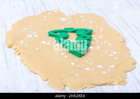 Weihnachten und Neujahr Tradition. Familienhaus Bäckerei. Kochen traditionelle Lebkuchenkekse. Plastikschneider in Form eines Weihnachtsbaums auf Dou Stockfoto