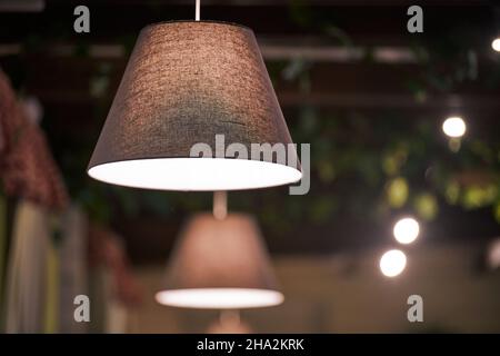 Pendelleuchten über Tischen im Café der Stadt, Restaurant mit Abendbeleuchtung. Beigefarbene Lampenschirme mit schwach gedimmtem warmem Licht. Moderne Innenausstattung, Pendelleuchte Stockfoto