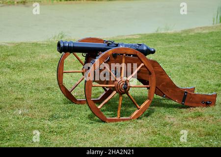 Restaurierte Kanone Modell für Burg Verteidigung, grünen Rasen Hintergrund. Artillerie Großkalibergewehr, alte alte Kanone auf Holzrädern. Schützen Sie sich vor att Stockfoto