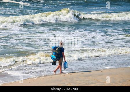 Junge Backpacker-Frau, die auf dem Meer unterwegs ist. Mädchen Reisende mit großen blauen Rucksack erkunden neue Region, schöne Ostsee Hintergrund. Solo weiblich Stockfoto
