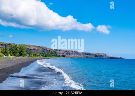 Schöne Aussicht auf schwarzen Sandstrand mit Bergen unter dem blauen Himmel, Saint Paul, Reunion, Frankreich Stockfoto