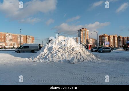 Auf einem Parkplatz auf der Straße liegt nach einem Schneefall ein großer Haufen Schnee mit Wohngebäuden im Hintergrund. Stockfoto