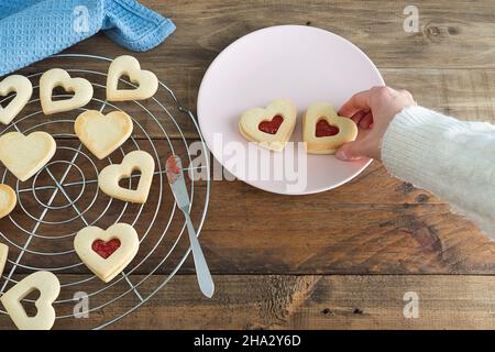 Frauenhand, die herzförmige Kekse auf den Teller legt. Speicherplatz kopieren. Valentinstag-Konzept. Stockfoto