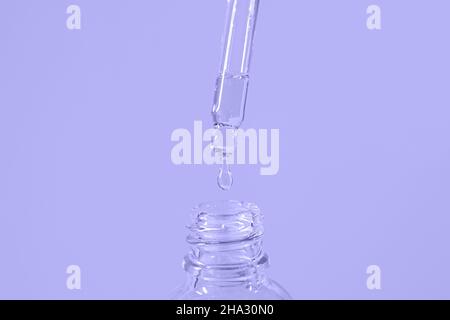 Flüssigkeit tropft von der Pipette in die Flasche in der trendigen Farbe von 2022 Very Peri Stockfoto