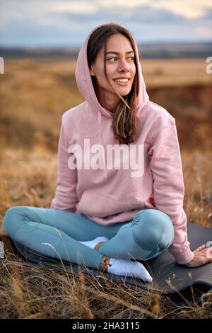 Erwachsene Frau, die sich während des Yoga-Trainings, der morgendlichen Routine, des Sonnenaufgangs, im Freien auf der Fitnessmatte entspannt. Junge Sportlerin in Sportswear, die sich in der Natur dehnt Stockfoto