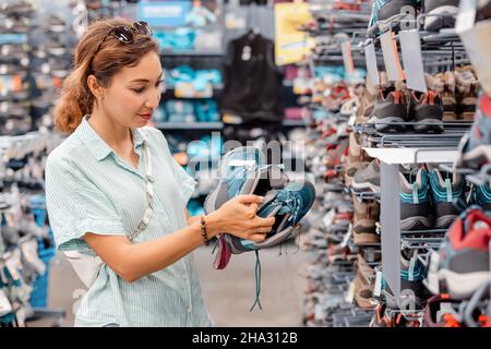 Kundin, die moderne Wanderschuhe aus Synthetikmaterial mit atmungsaktiver und wasserdichter Membran auf der Ladenfläche wählt Stockfoto