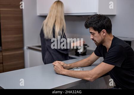Junge kaukasische Frau und bärtiger Mann reden nicht nach Streit, in der Küche, frustrierte blonde Frau und Mann ignorieren einander, Beziehung Profi Stockfoto
