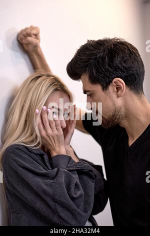 Mann attackiert Frau, häusliche Gewalt. Betrunkener Ehemann schlägt Ehefrau. Ein aggressiver Mann trifft verängstigtes Weibchen und weint. An die Wand geklemmt und verängstigt. Famil Stockfoto