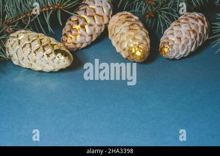 Neujahrshintergrund auf blau. Zweige Tannenbaum mit goldenen Weihnachtszapfen. Leerzeichen für Text Stockfoto