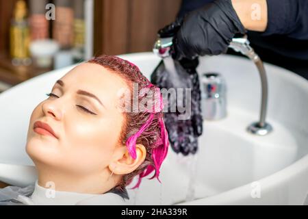 Waschen gefärbte weibliche Haare. Professioneller Friseur wäscht rosa Farbe Farbe von einem Kunden. Die junge kaukasische Frau ließ sich in einem Schönheitssalon die Haare waschen Stockfoto